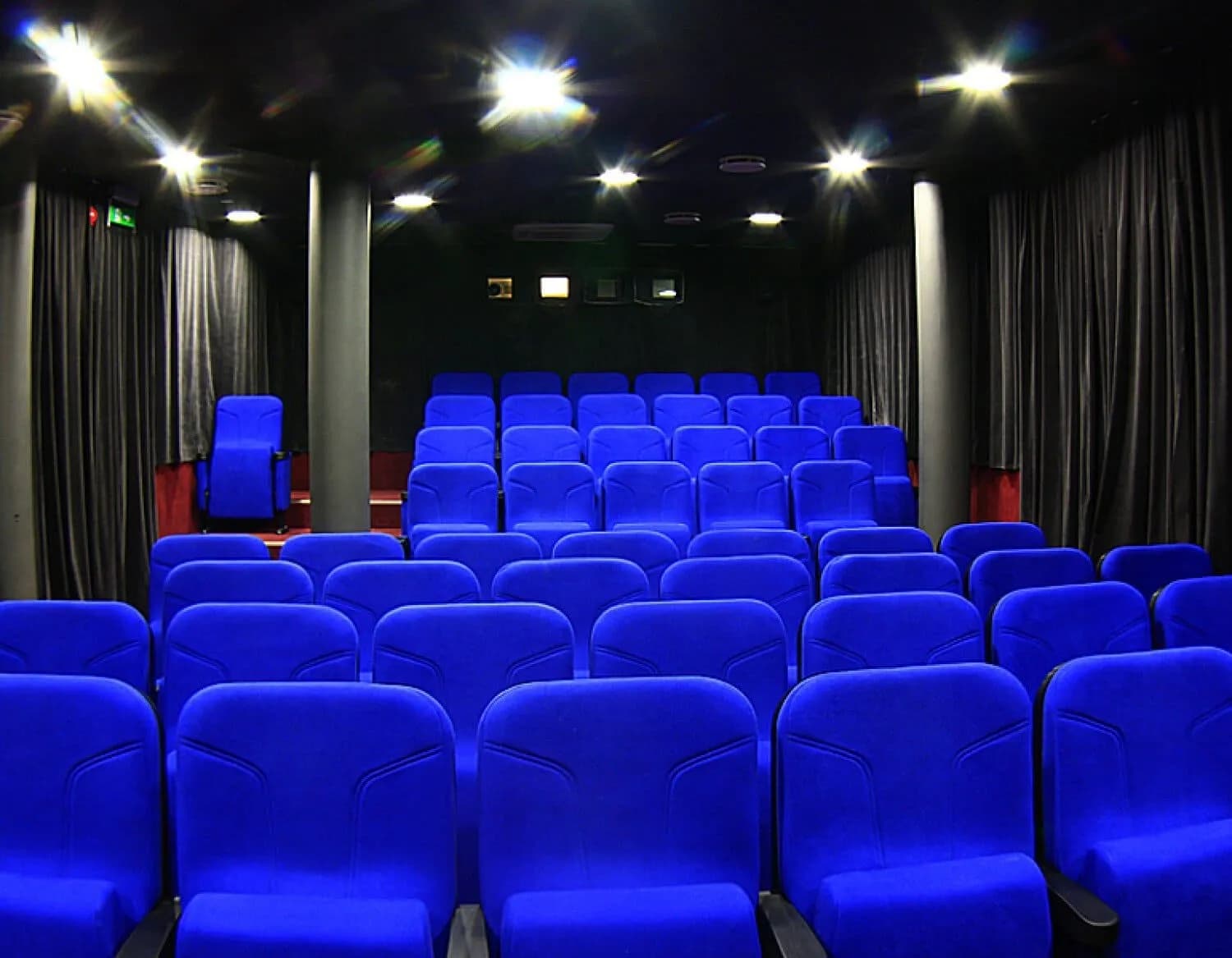 A perspective view of empty blue cinema seats in a dark movie theater with dimmed lights.